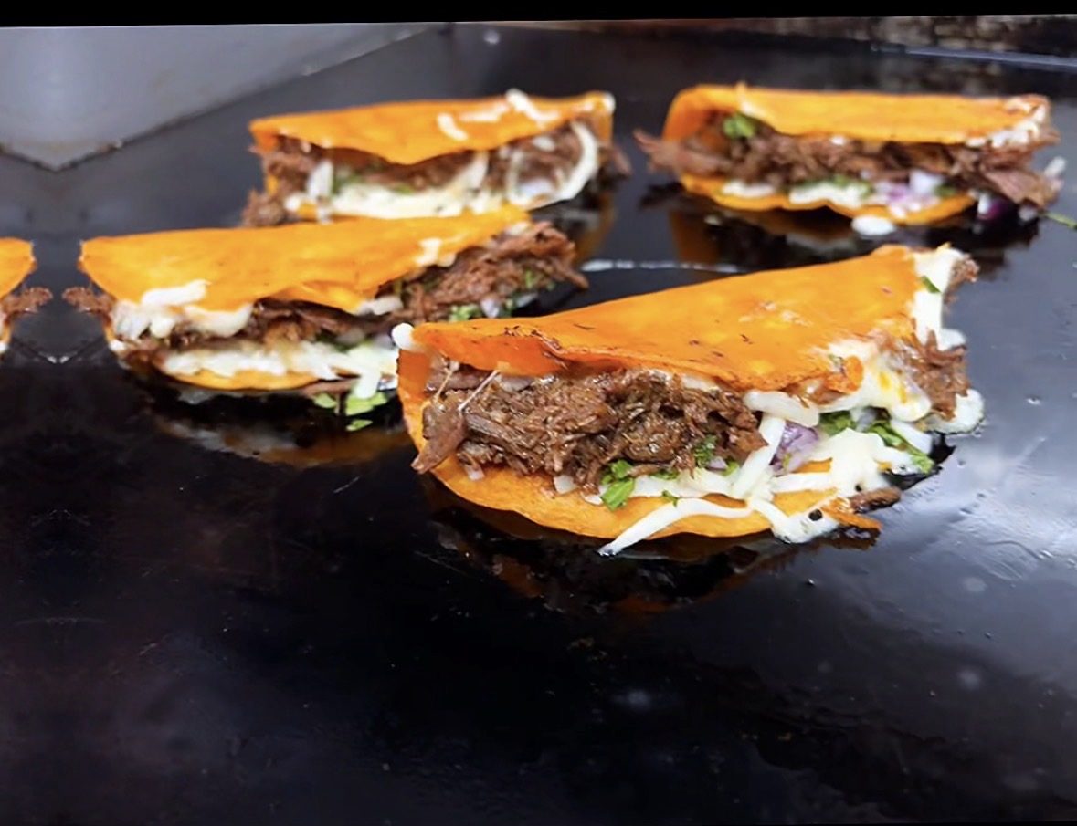 Quesabirria tacos crisping on the flat-top griddle inside the Guat-A-Taco food truck